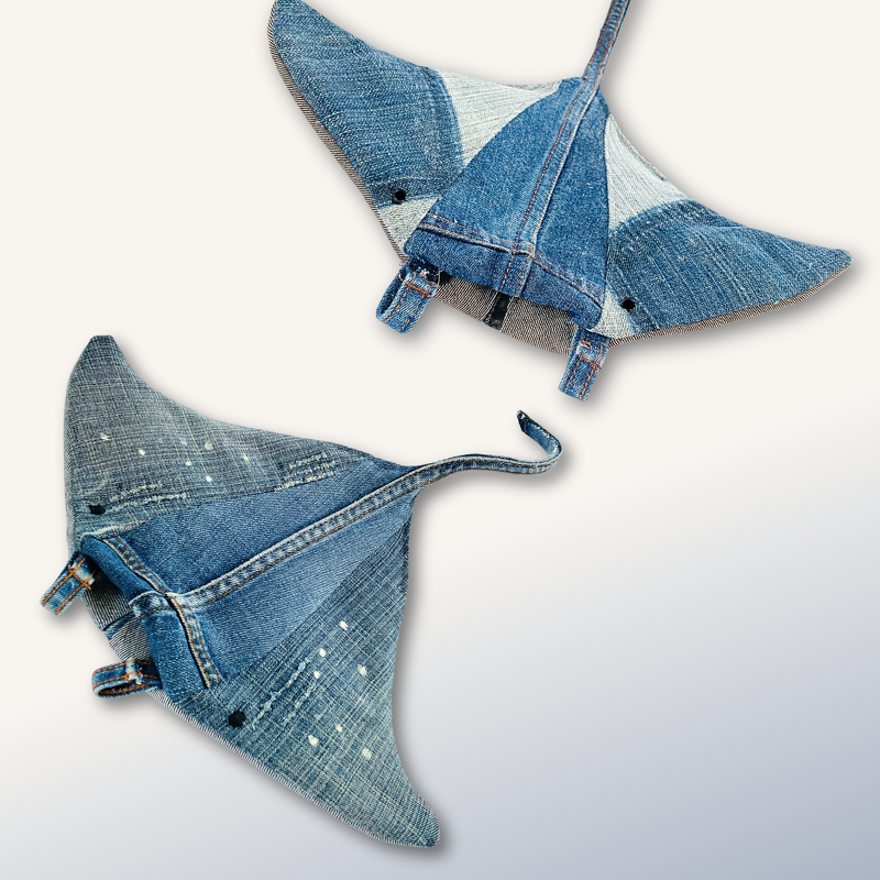 Two manta ray-shaped denim potholders in blue tones, one paint-splattered and one patchwork, on a light background.