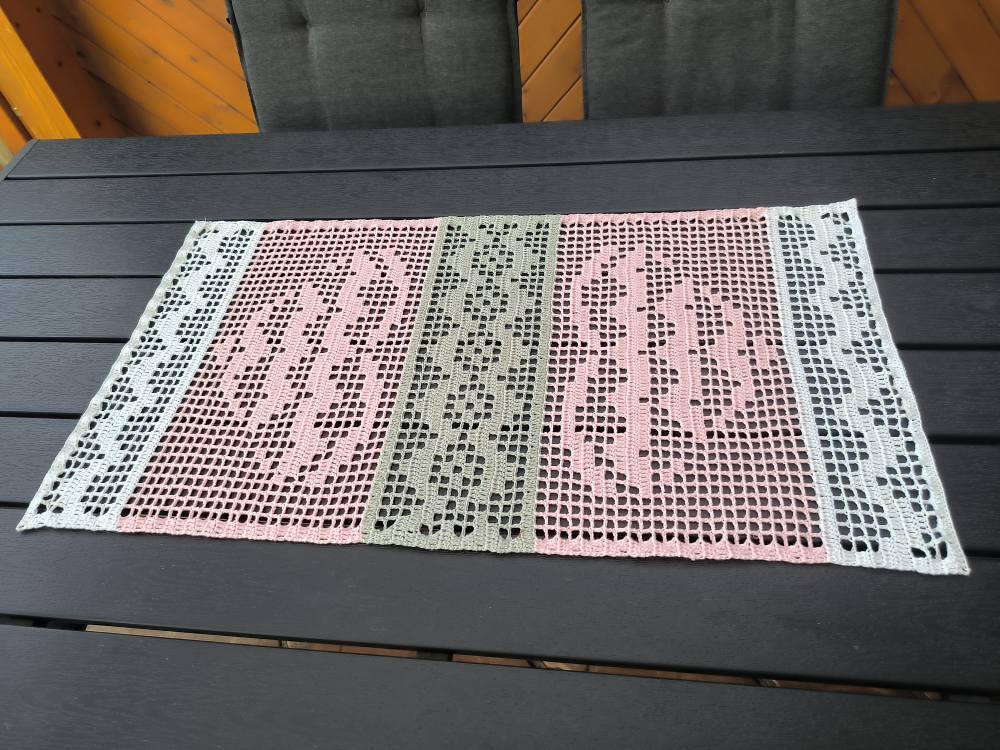 Rechteckiger gehäkelter Tischläufer in Filettechnik, Rosé, Grün und Weiß, auf dunklem Holztisch ausgebreitet.