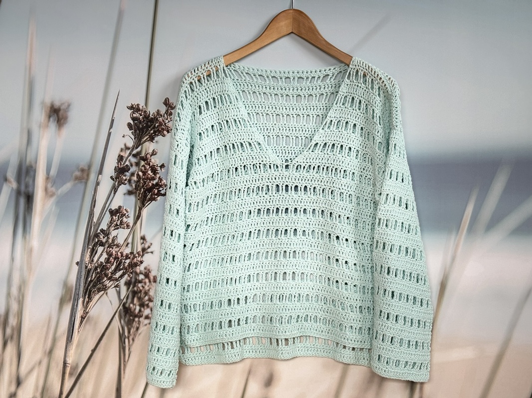 Boxy mint crochet sweater with V-neck and rectangular eyelet stitch rows hanging on a wooden hanger