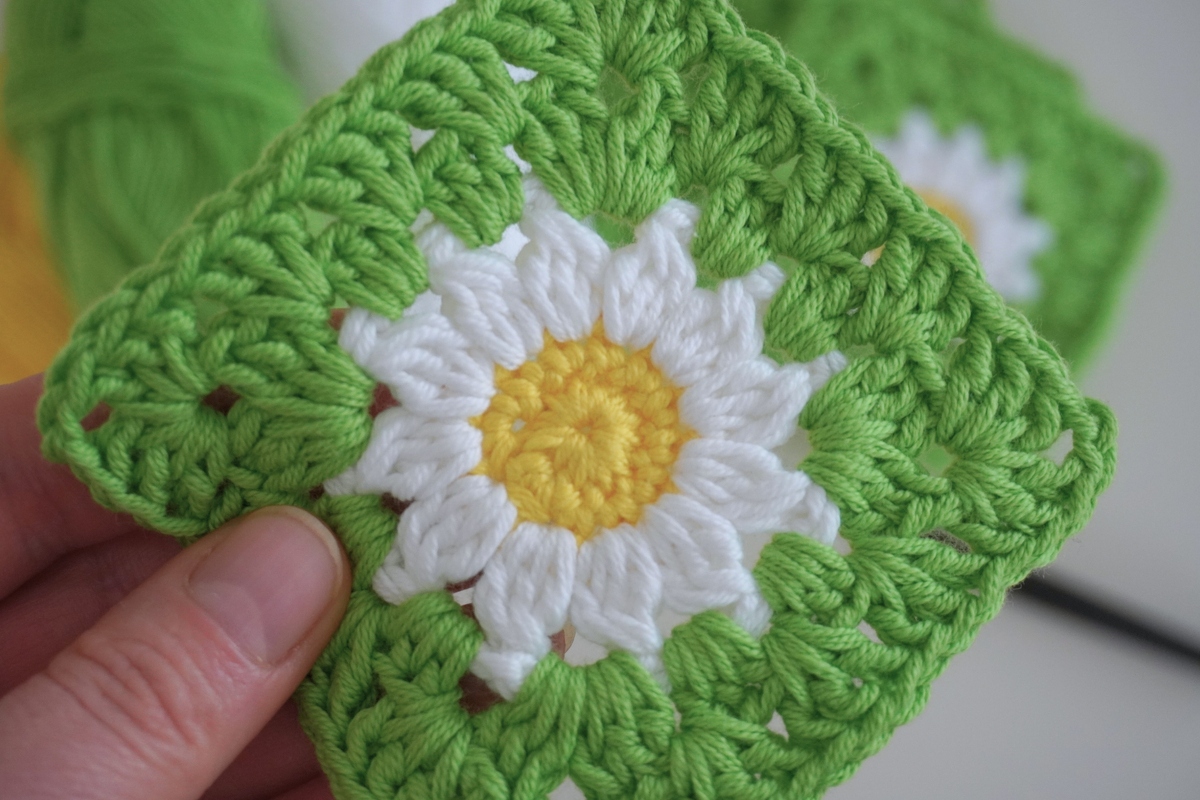 White and yellow daisy granny square with green border held between fingers