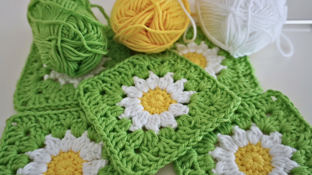 Close-up of crochet daisy granny squares in green with white petals and yellow centers, with matching yarn balls