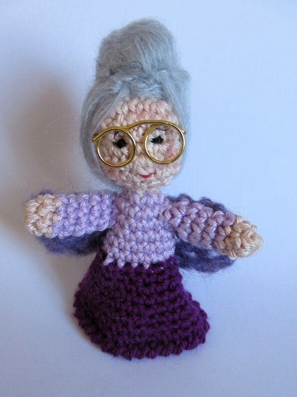 Gehäkelte Amigurumi-Oma mit Dutt und runder Brille auf hellem Hintergrund