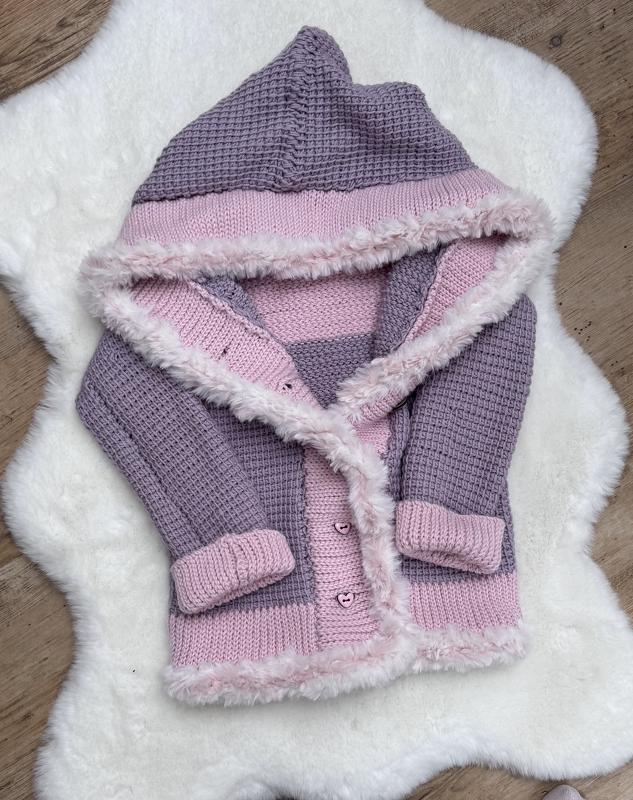 Gehäkelte Kapuzenjacke in Rosa und Lila mit Kunstfellrand und herzförmigen Knöpfen auf hellem Untergrund