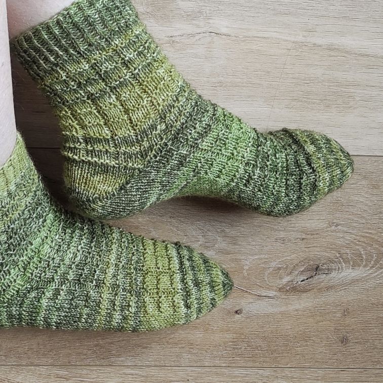 Handgestrickte grüne Socken mit Rippenmuster auf Holzboden