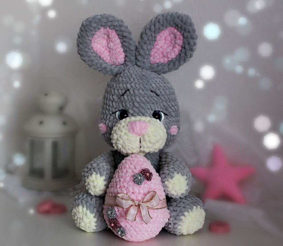 Gehäkelter grauer Hase mit rosa Ei und Schleife, sitzend