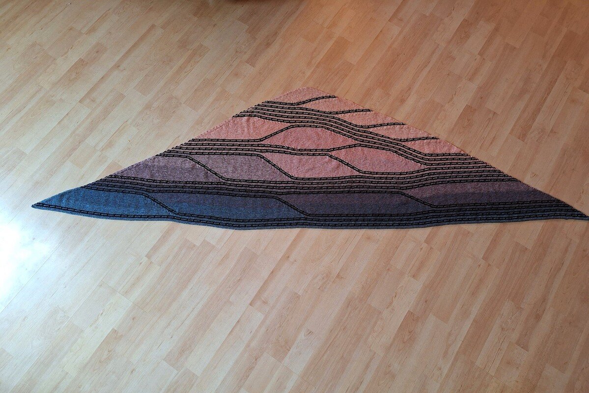 Gestricktes Dreieckstuch mit blau-rosa Farbverlauf und schwarzen Wellenlinien auf hellem Boden