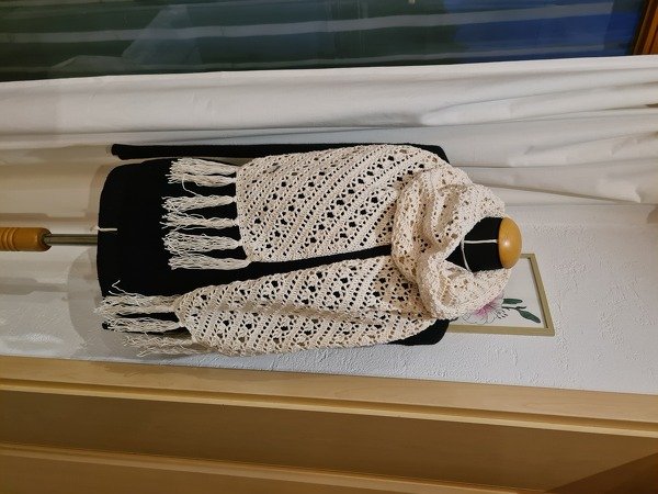 Cremefarbener gehäkelter Schal mit diagonalem Lochmuster und langen Fransen auf schwarzer Schneiderpuppe