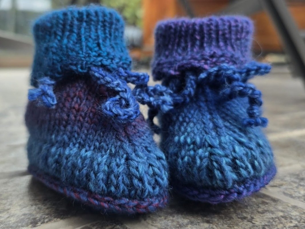 Gestrickte Babyschuhe in Blau-Lila-Farbverlauf mit Umschlagbündchen und Bindeband