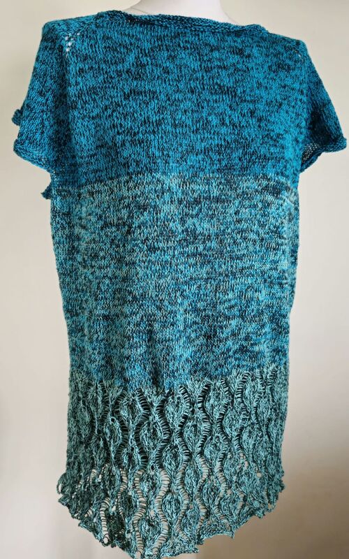 Rückansicht einer gestrickten Damen-Tunika in Türkis-Blau mit kurzem Ärmel und offenem, wellenförmigem Lochmuster am Saum