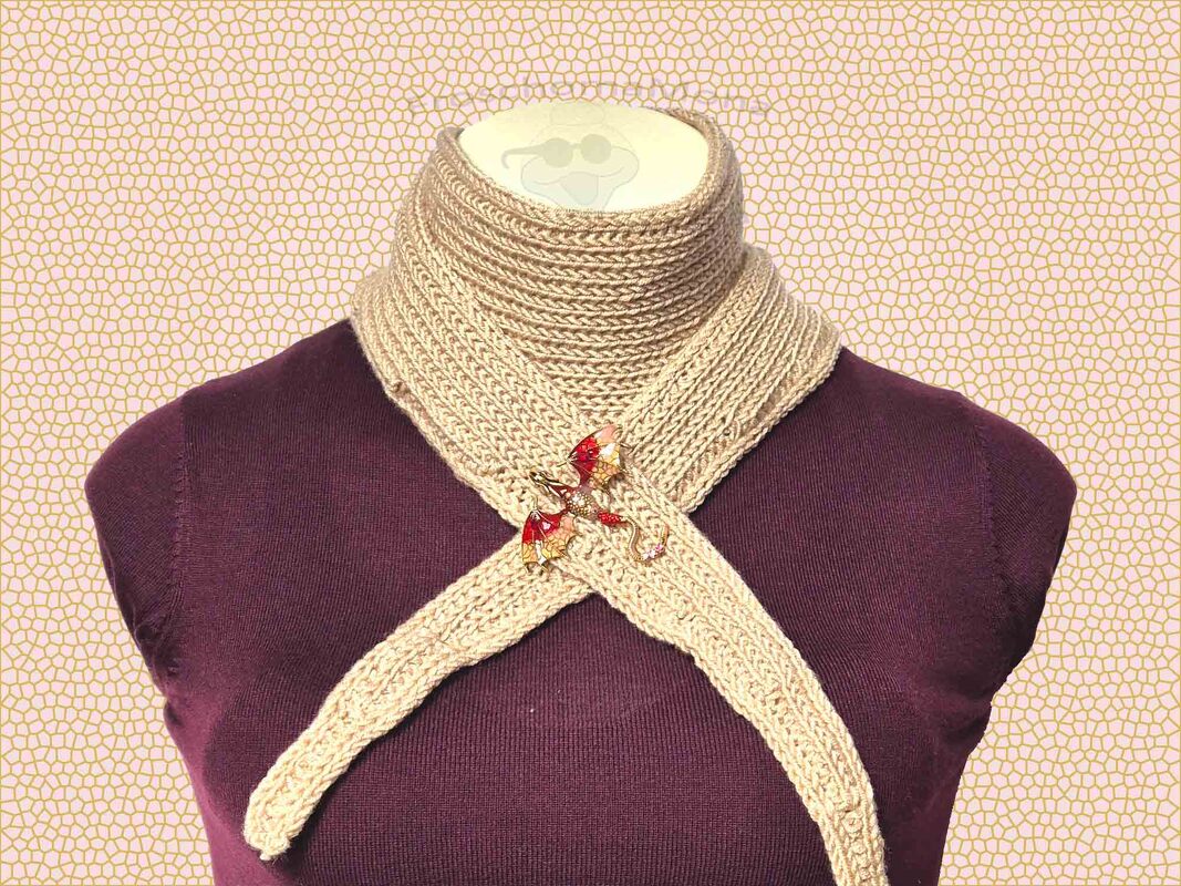 Schmales cremefarbenes gestricktes Dreieckstuch, gekreuzt am Hals einer Büste, mit rot-goldener Drachenbrosche.