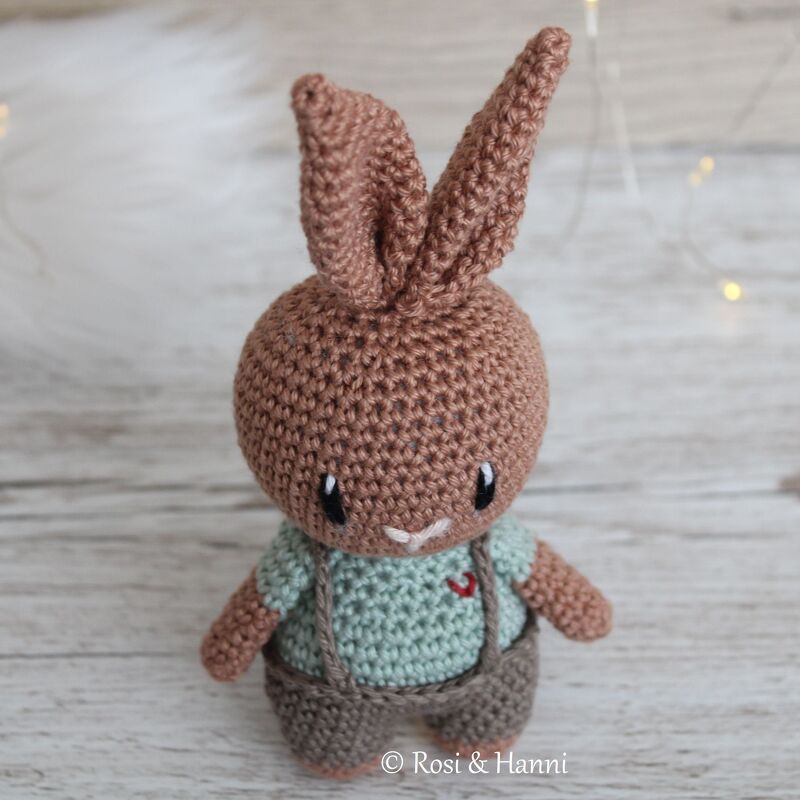 Brauner gehäkelter Amigurumi-Hase mit langen Ohren, mintgrünem Shirt und brauner Latzhose