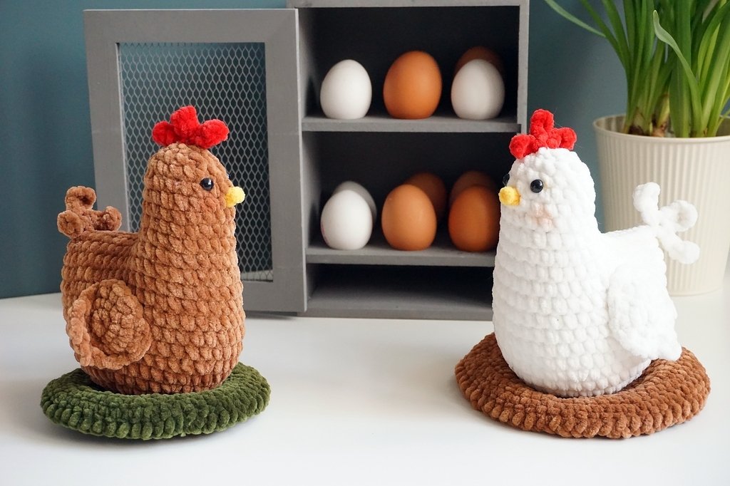 Zwei gehäkelte Amigurumi-Hühner, braun und weiß, auf runden Unterlagen vor einem Eierregal
