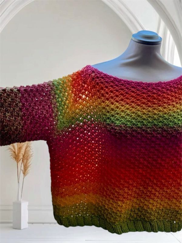 Gehäkelter Damenpullover in Regenbogenfarben mit offenem Lochmuster auf Schaufensterpuppe.