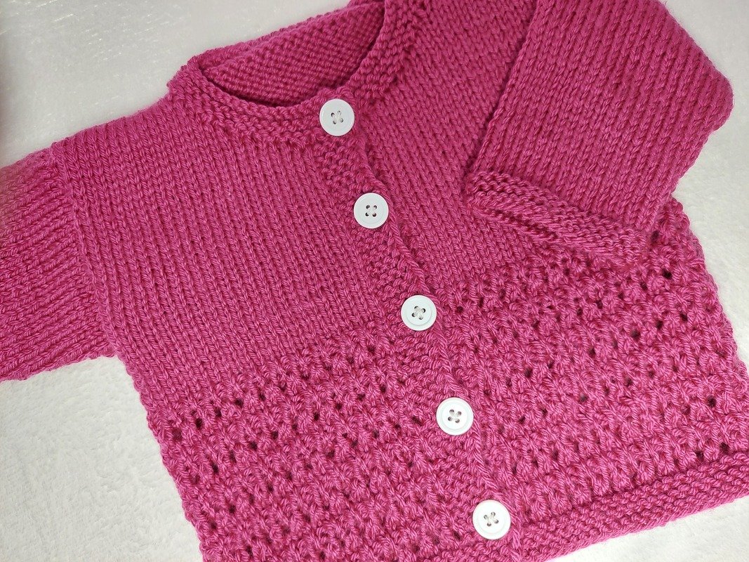 Rosafarbene handgestrickte Babystrickjacke mit weißen Knöpfen und Lochmuster