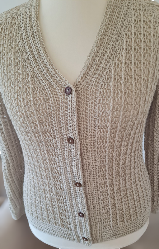 Beige gehäkelte Damenjacke mit V‑Ausschnitt und braunen Knöpfen auf Schneiderbüste