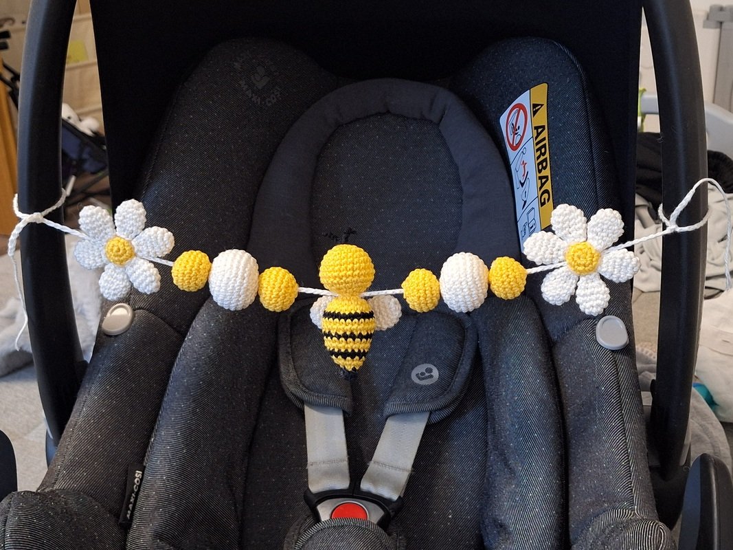Yellow and white crocheted garland with a striped bee and two daisies tied across a dark infant car seat handle