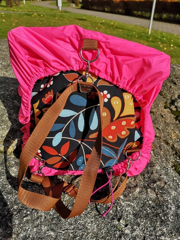 Rucksack mit pinker Regenhülle und floralem Muster auf Felsen