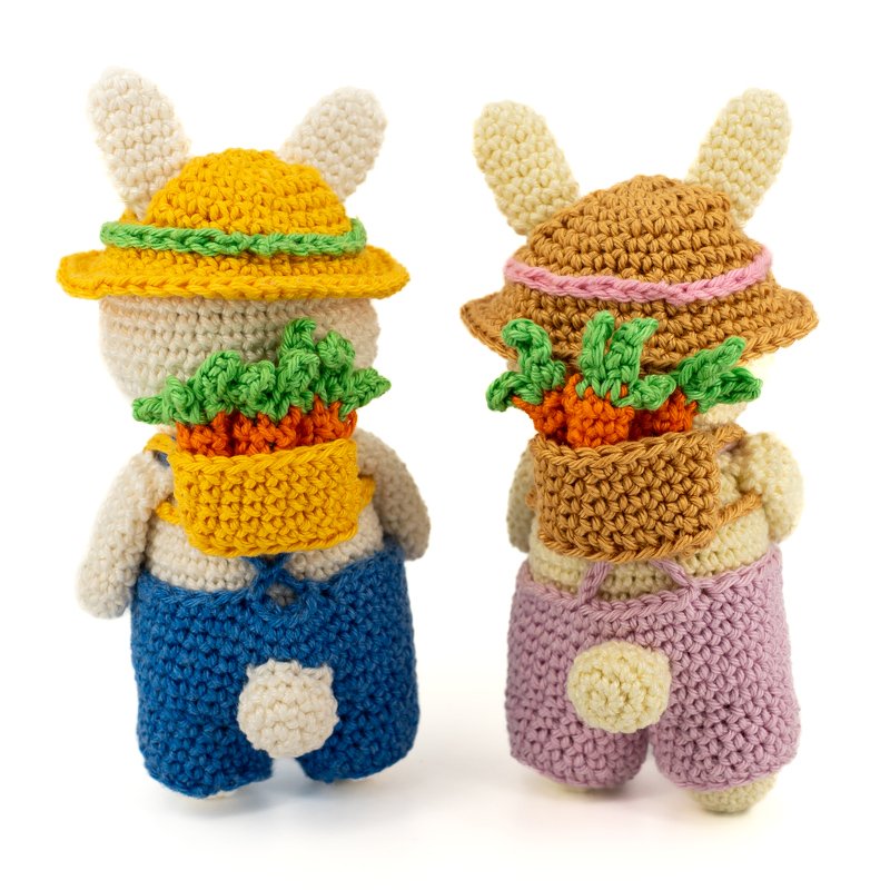 Rückansicht von zwei gehäkelten Amigurumi-Hasen in Latzhosen, mit Strohhüten und Rucksäcken voller gehäkelter Karotten
