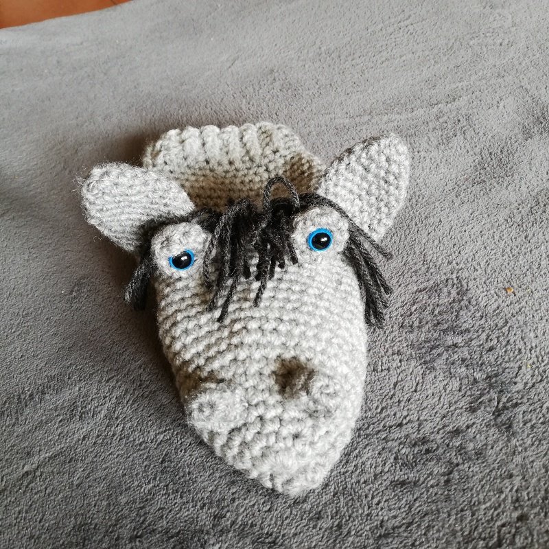 Gehäkelte Pferde-Handpuppe mit blauen Augen und dunkler Mähne auf grauem Untergrund