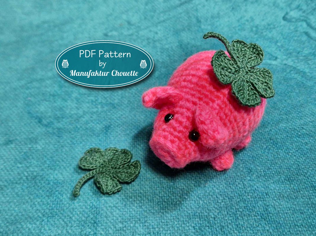 Rosa gehäkeltes Amigurumi-Glücksschwein mit grünem vierblättrigen Kleeblatt auf türkisfarbenem Hintergrund.