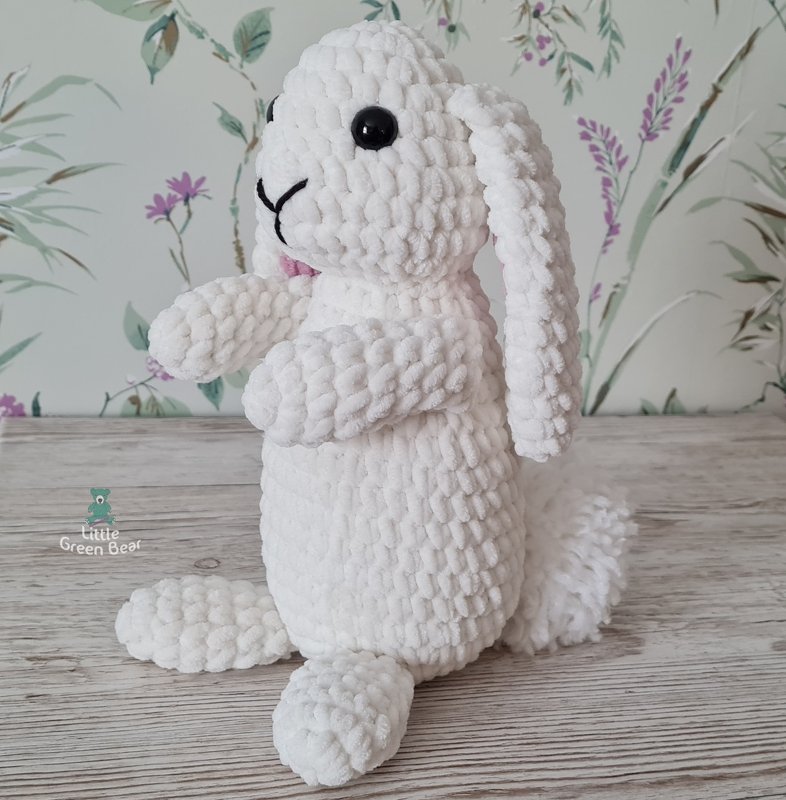 White crocheted amigurumi bunny with black eyes, embroidered nose and floppy ears, sitting on a wooden surface.