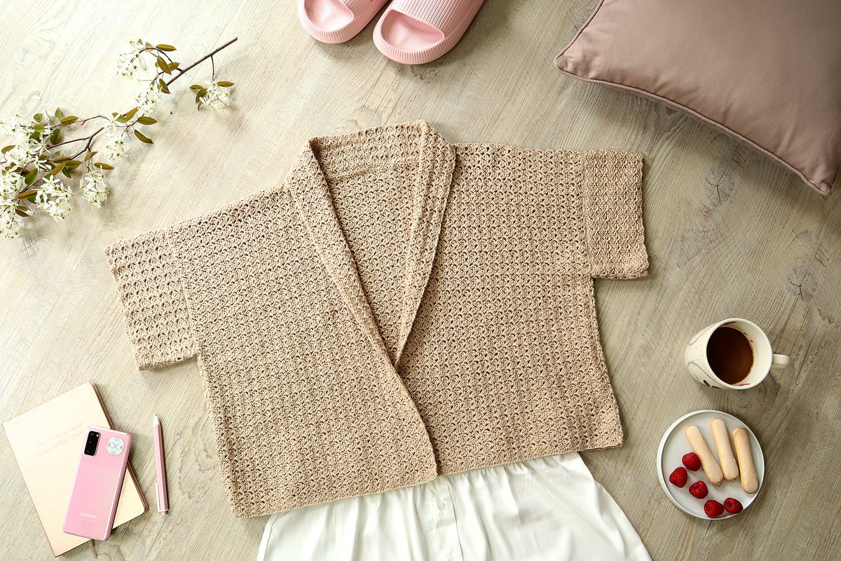 Beige short-sleeve crochet women's jacket with shawl collar laid flat on a wooden surface