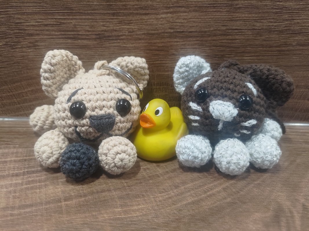 Beiges Amigurumi mit Schlüsselring, braunes Amigurumi mit weißen Akzenten und eine gelbe Quietscheente auf Holz