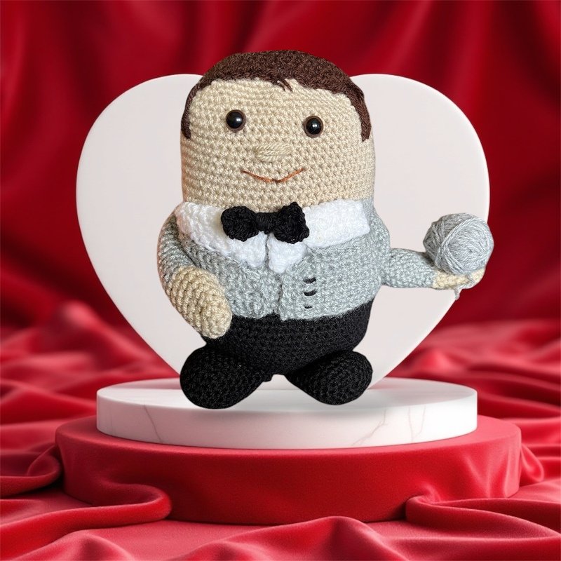 Gehäkelte Amigurumi-Puppe mit grauem Sakko, schwarzer Fliege und Wollknäuel vor rotem Hintergrund