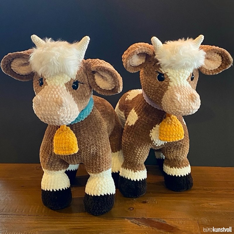 Two crocheted brown-and-white amigurumi cow plushies wearing collars with small yellow bells.