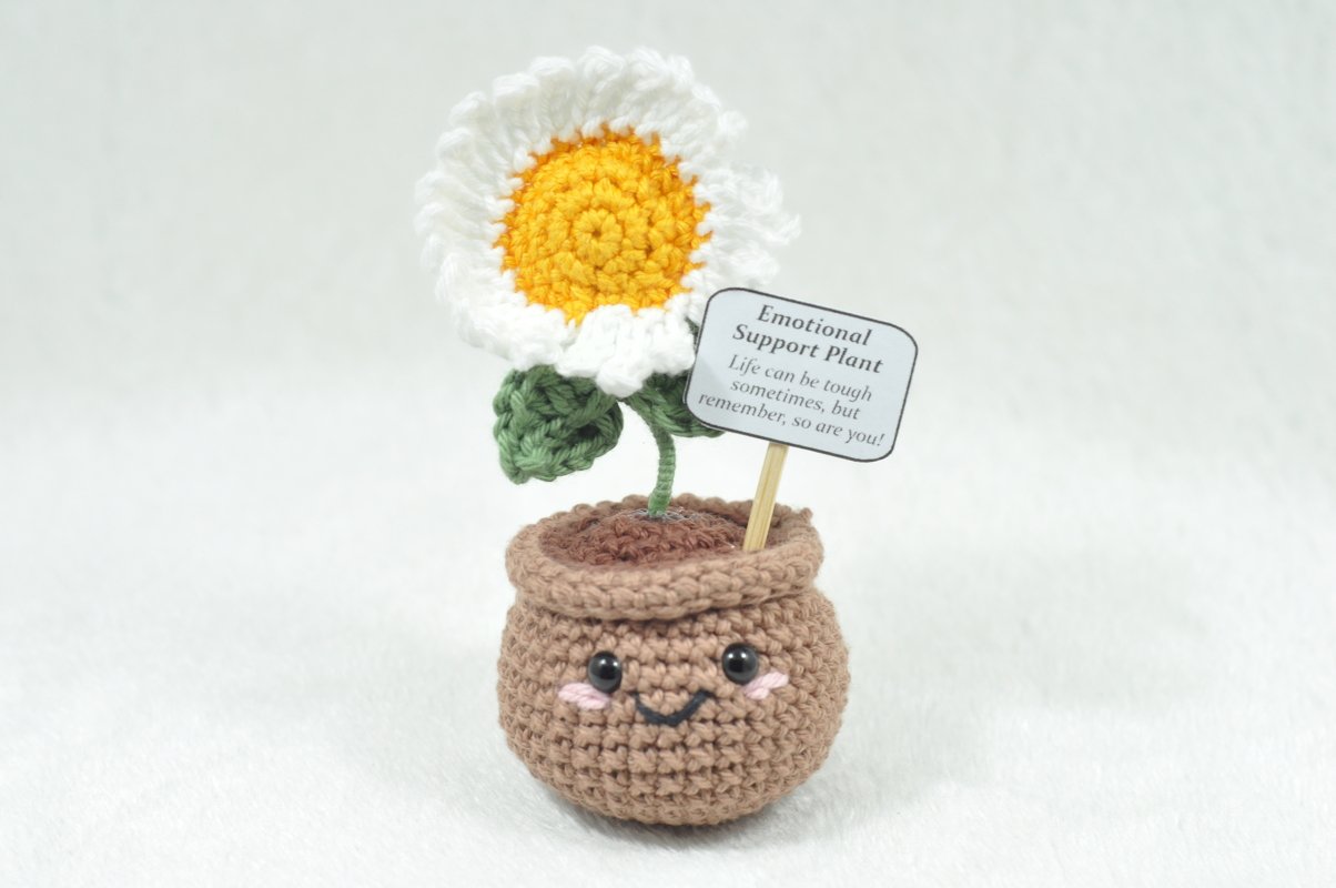 Cheerful crocheted daisy in a small pot with a sign that reads 'Emotional Support Plant'.