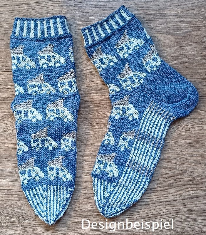 Paar blauer, gestrickter Socken mit weißem Auto-Muster und gestreifter Sohle auf Holz; Schriftzug ‚Designbeispiel‘