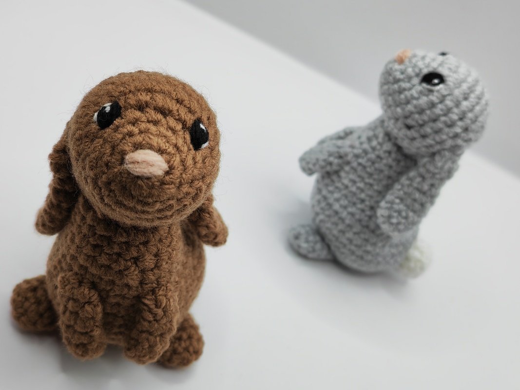 Two cozy crochet bunnies, brown at left and grey at right, standing on a white background