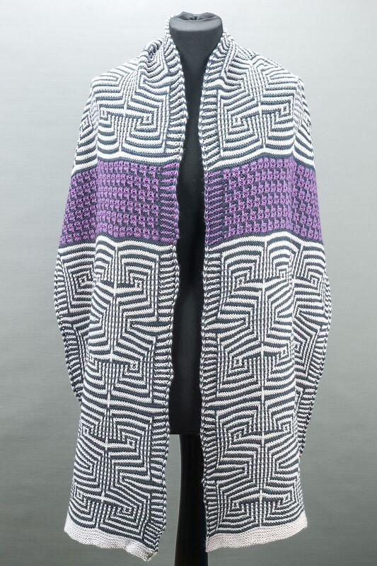 Knitted black-and-white geometric shawl with a textured purple band draped over a black dress form