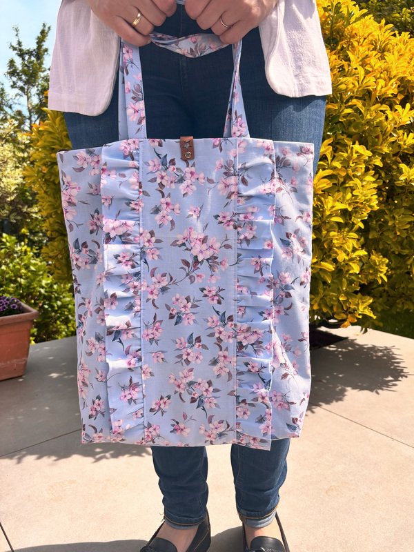 Hellblaue Einkaufstasche mit rosa Blumenmuster und vertikalen Rüschen