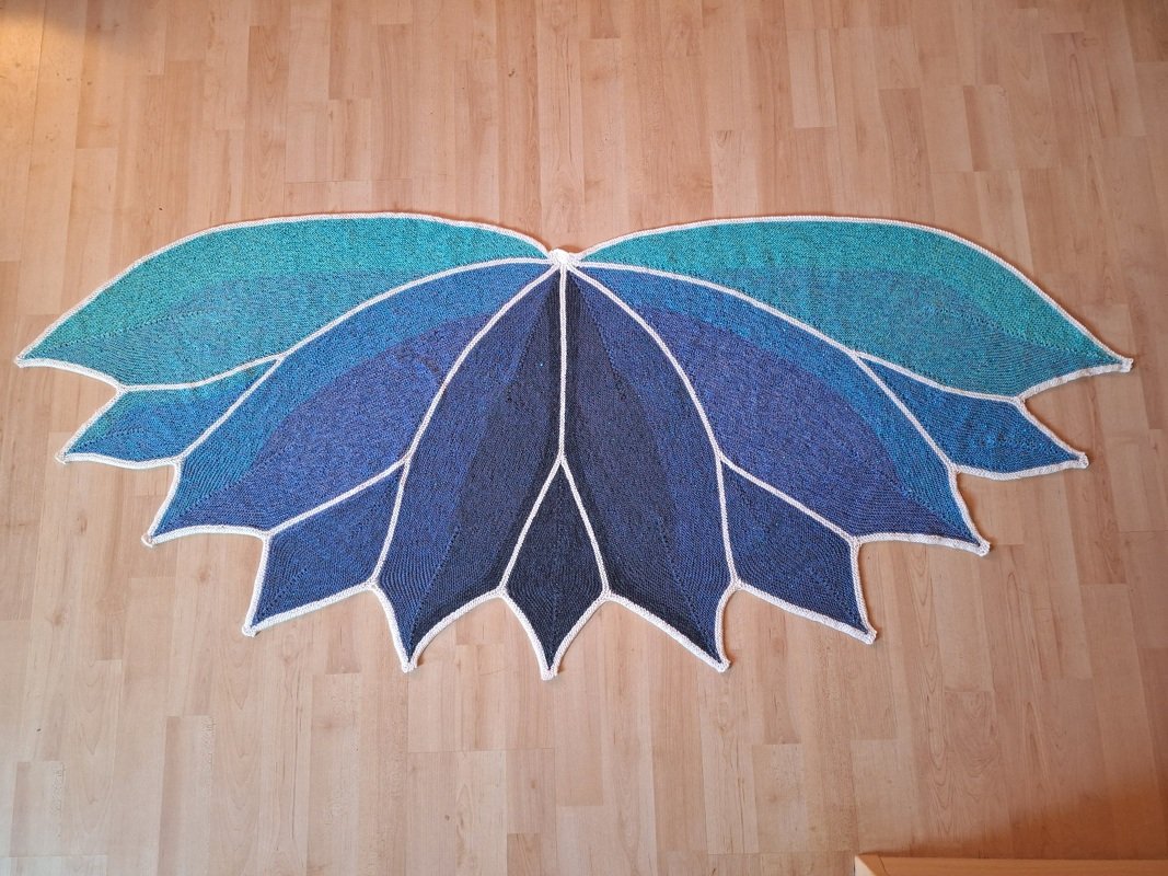 Halbrundtuch mit blauen und türkisfarbenen Blattsegmenten, weiße Einfassung, auf hellem Holzfußboden ausgebreitet