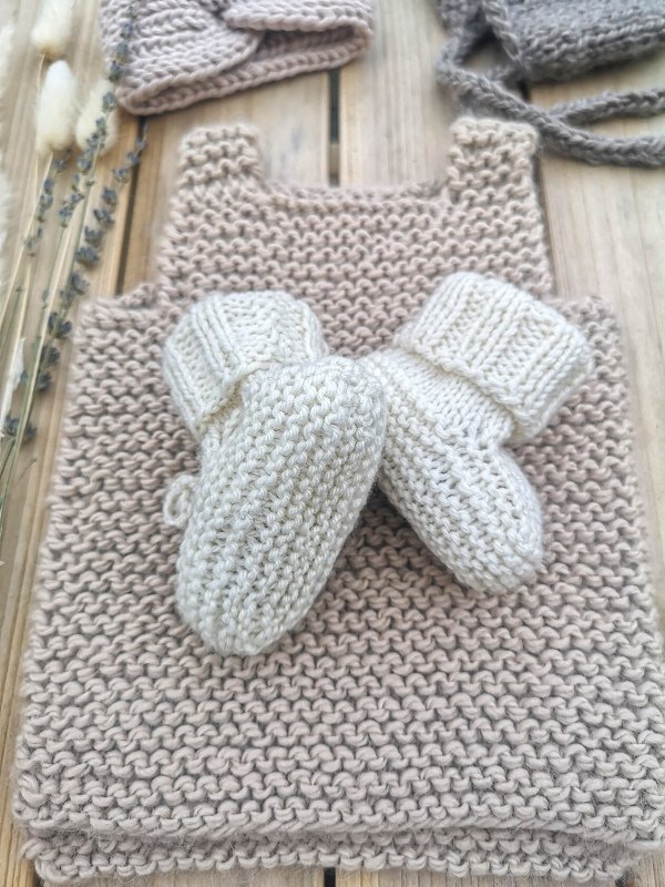 Cremefarbene gestrickte Babyschuhe mit Umschlagbündchen auf beigefarbenem Stricktuch