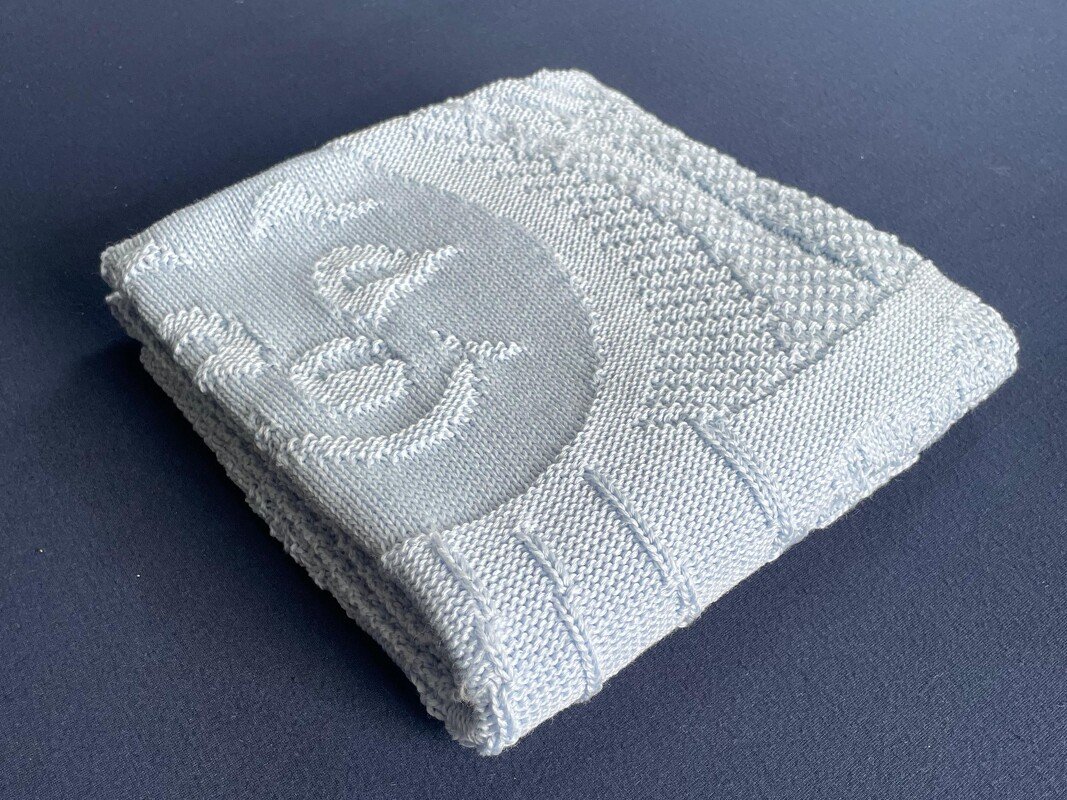 Folded pale blue knitted baby blanket with ribbed edge and raised stitch pattern