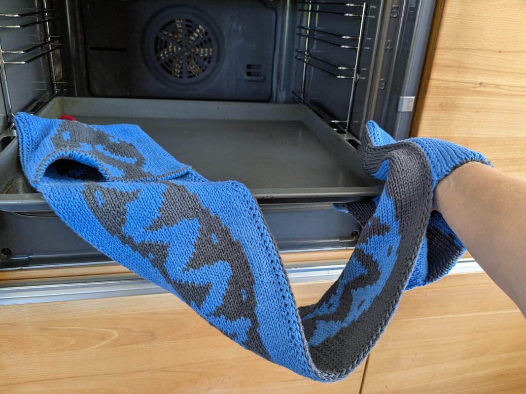 Hand mit langem blau-grauem Topflappen zieht Backblech aus dem Ofen