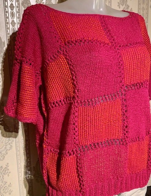 Gestrickte Tunika in Rot- und Pinktönen mit Quadratmuster auf einer Schaufensterpuppe