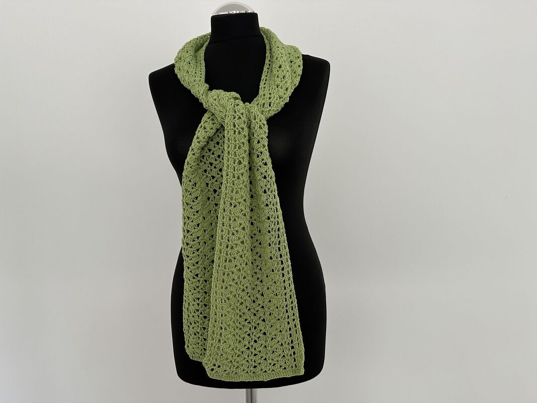 Lindgrüner gehäkelter Schal mit Lochmuster an einer schwarzen Schaufensterpuppe, vorne locker geknotet