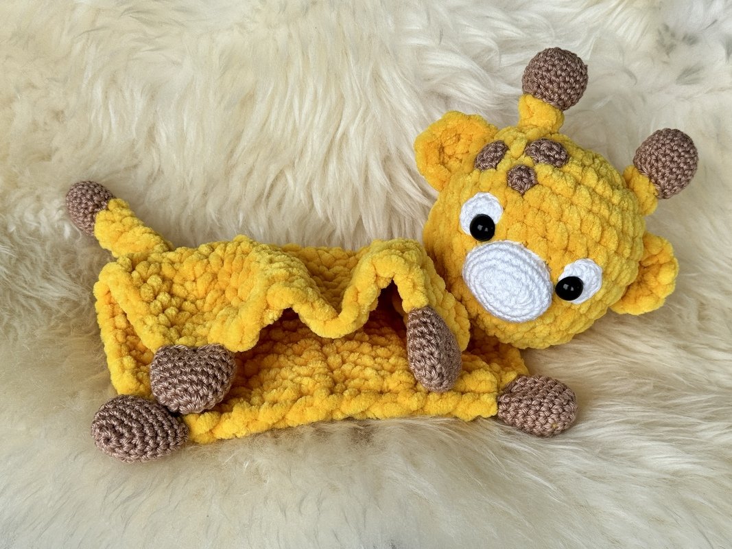 Yellow crocheted giraffe lovey with textured blanket on cream fur background