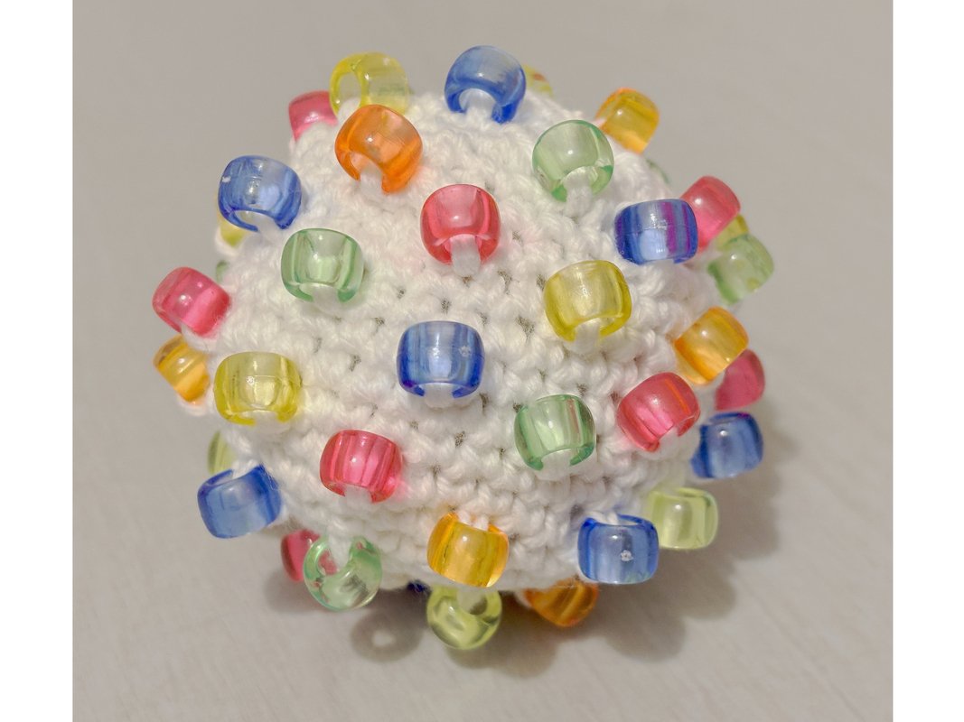 White crocheted ball covered in colorful translucent beads
