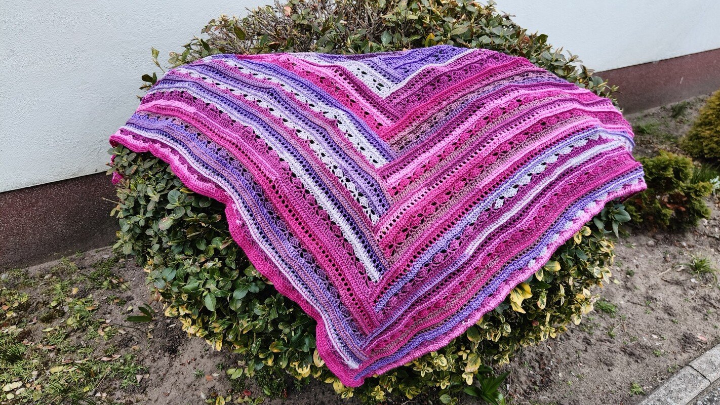 Gehäkeltes Dreieckstuch in Pink, Violett und Weiß auf grünem Strauch