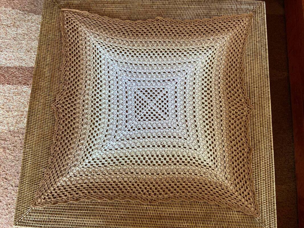 Quadratisches hellbeiges gehäkeltes Deckchen mit Filetmuster auf geflochtener Oberfläche