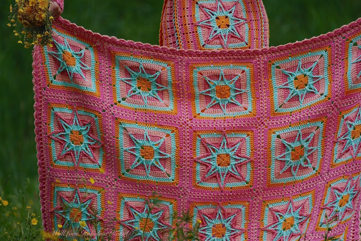 Farbenfrohe handgehäkelte Decke mit Stern‑Quadraten in Rosa, Türkis und Orange vor grünem Hintergrund.