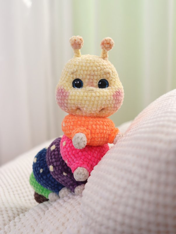 Gehäkelte bunte Amigurumi-Raupe mit schwarzen Augen und rosa Wangen
