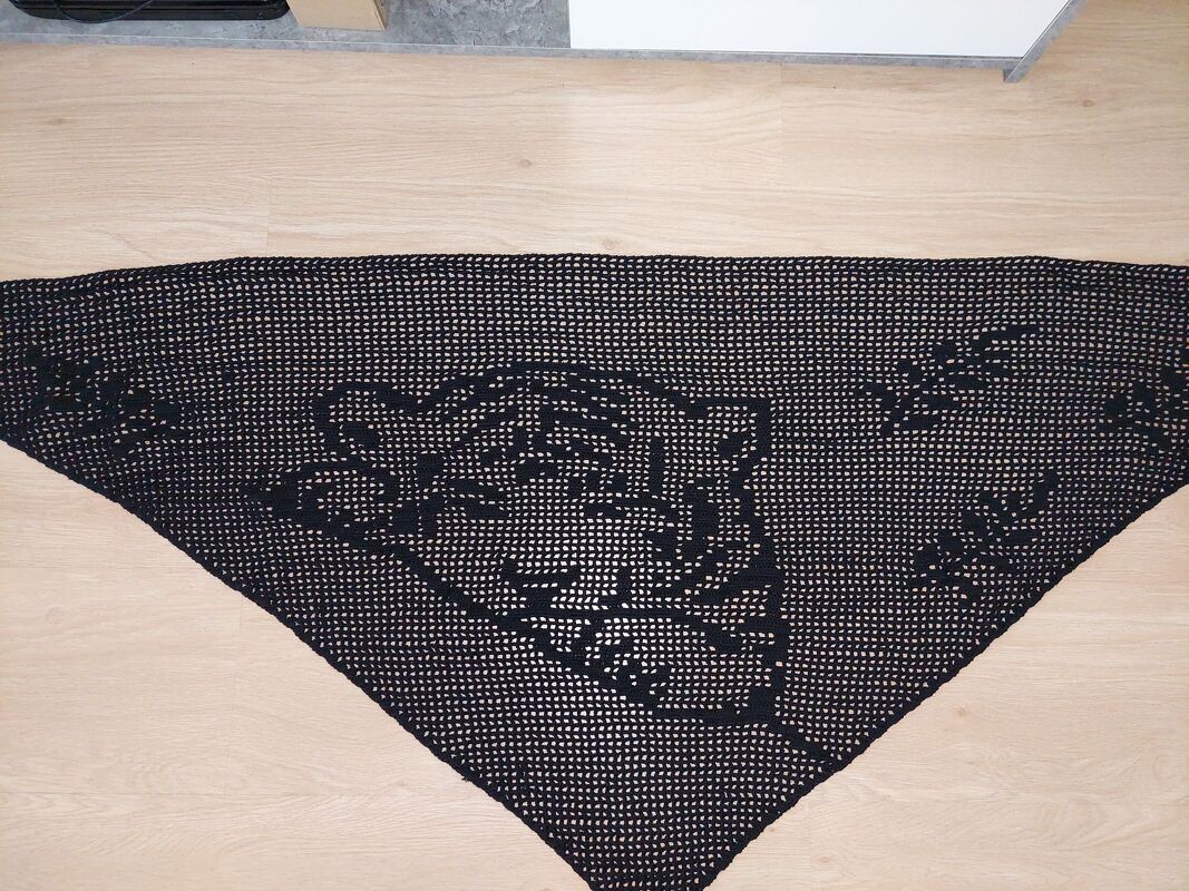 Schwarzes gehäkeltes Dreieckstuch mit Tigerkopf‑Motiv auf hellem Boden