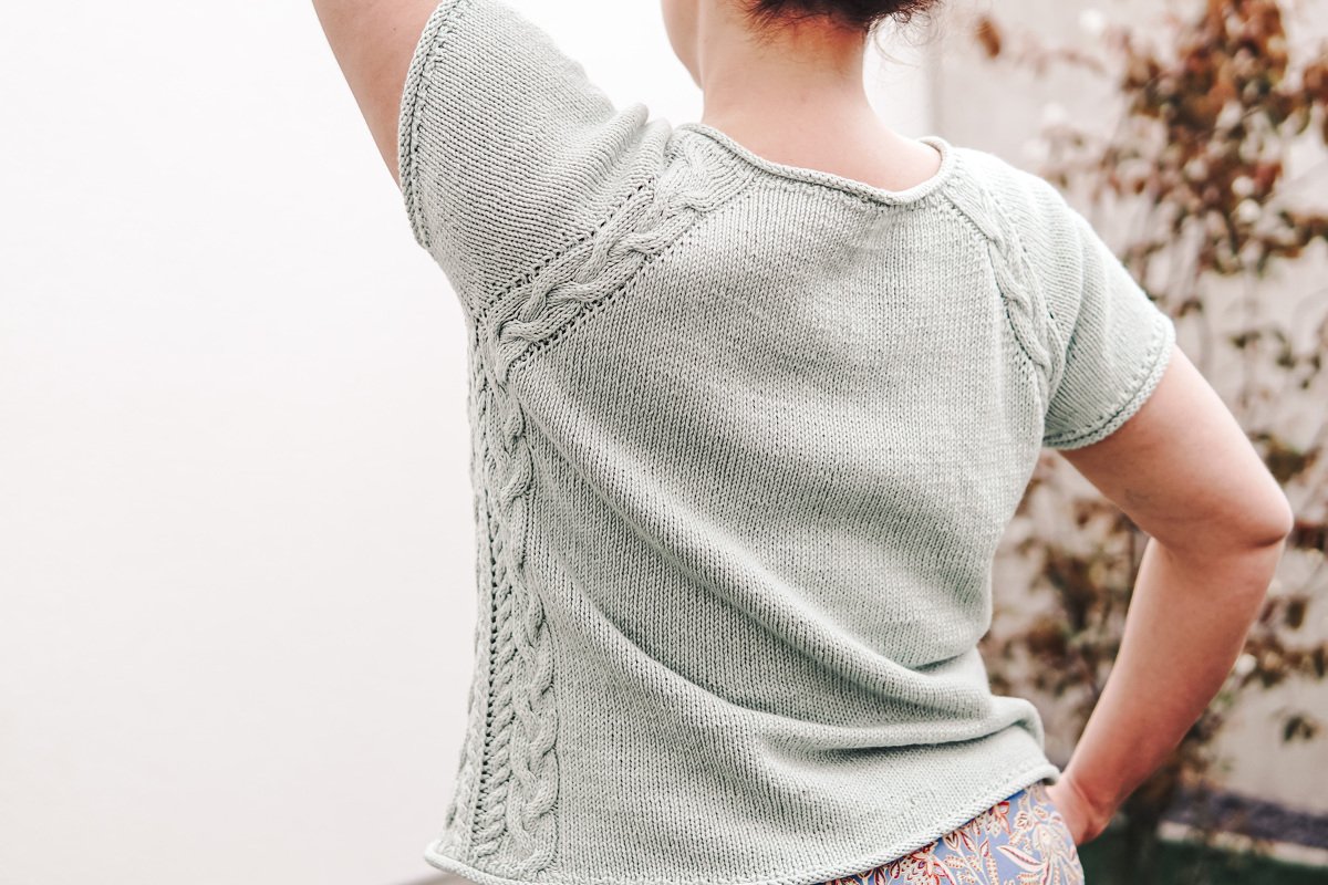 Back view of a person wearing a mint short-sleeve knitted top with cable side panels and raglan shaping