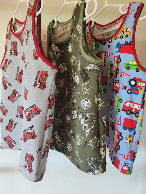 Drei ärmellose Kindershirts: grau mit Feuerwehrautos, olivgrün mit Grafikprints und hellblau mit bunten Fahrzeugen, hängend an weißen Bügeln.