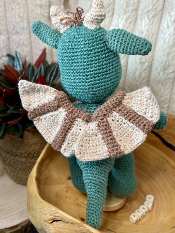 Gehäkelter petrolfarbener Amigurumi-Drache von hinten mit beiger-brauner Rüschenhalskrause und kleinen Hörnern